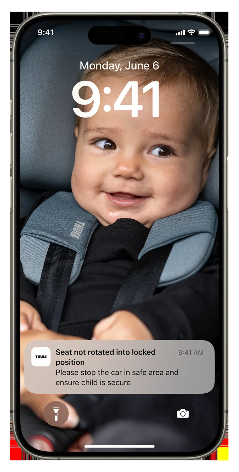 A phone lock screen showing a Thule car seat safety alert over a photo of a smiling baby