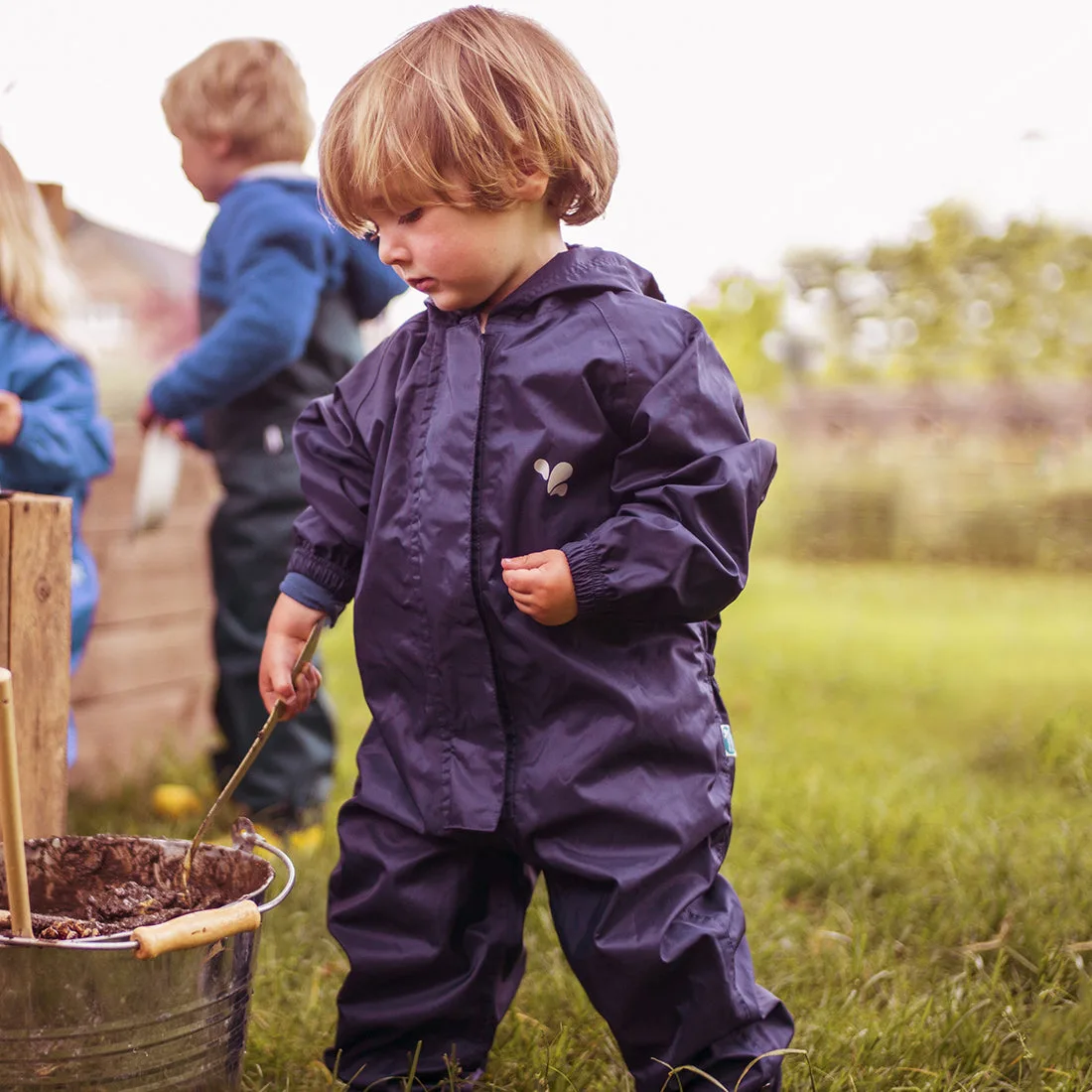 A child in a navy Muddy Puddles Originals waterproof puddle suit playing outdoors
