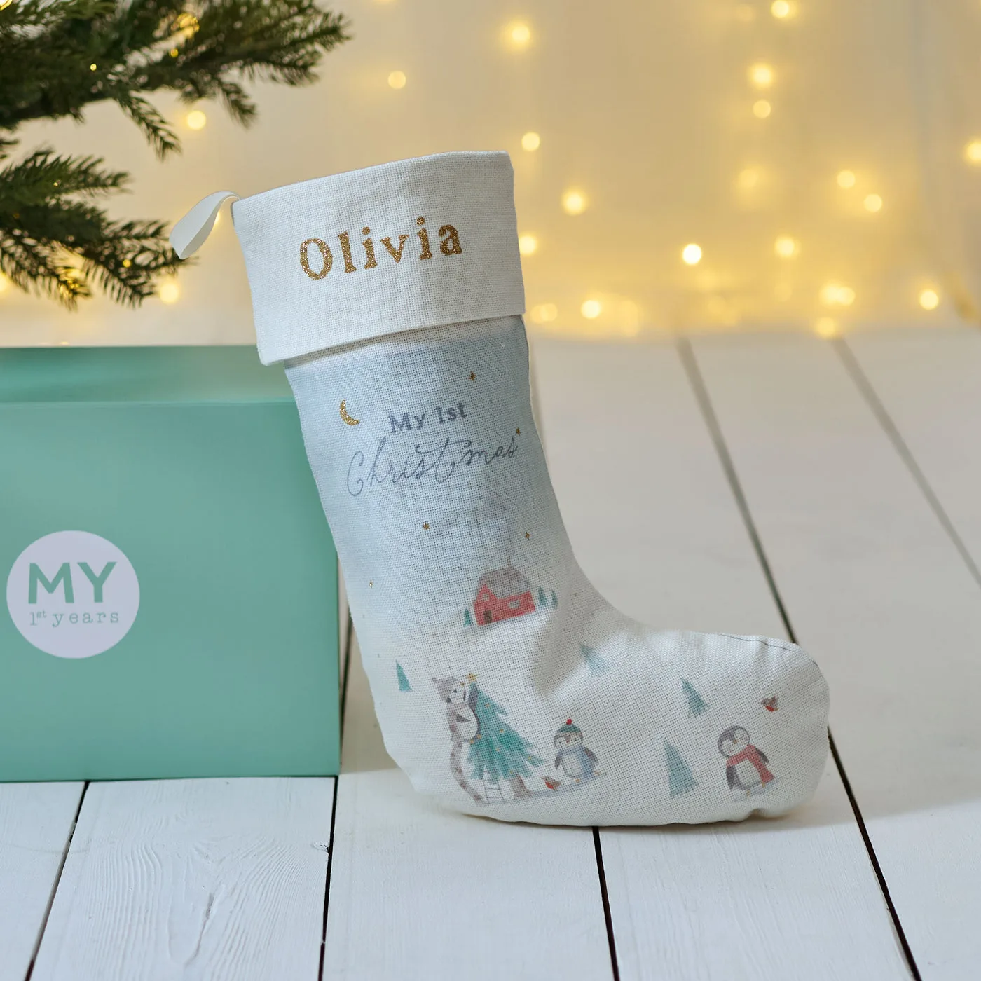 A small white My 1st Christmas stocking with a penguin scene and the name Olivia in gold, next to a mint My 1st Years gift box