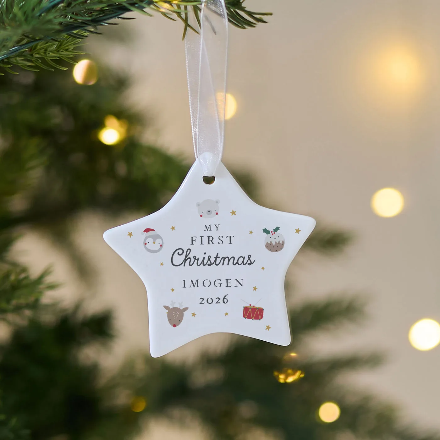 A white star-shaped ceramic My First Christmas decoration personalised with the name Imogen and the year 2026, hanging on a Christmas tree