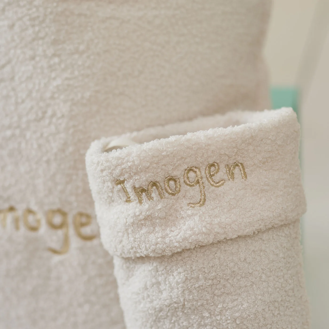 A cream borg Christmas sack and matching stocking, both embroidered with the name Imogen in gold, beside a Christmas tree