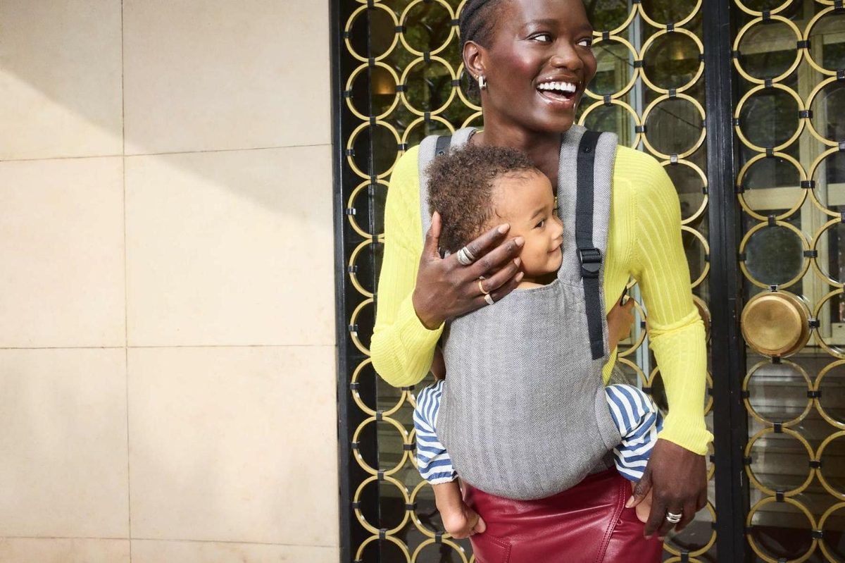 A smiling mum carrying her baby in a grey Tula Original carrier in Ash herringbone linen