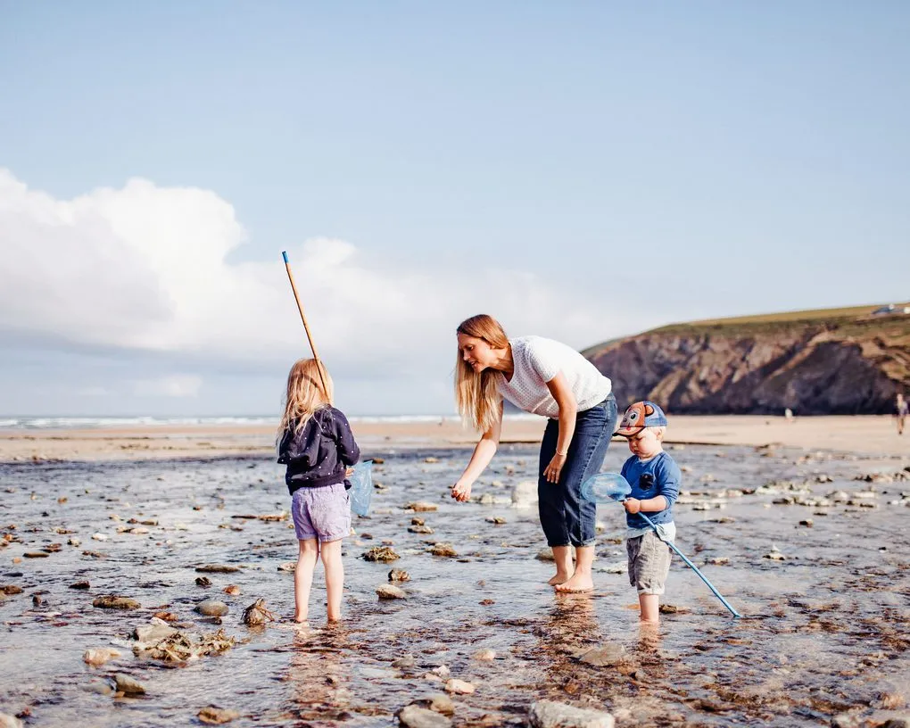 A mum and two children rock pooling on the beach at Mawgan Porth