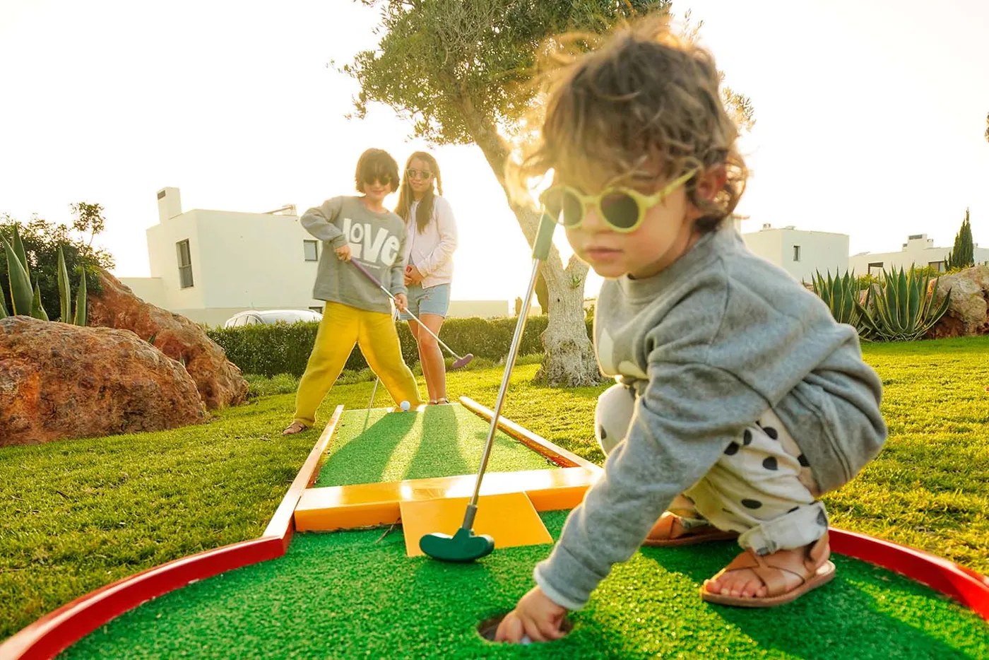 A toddler in sunglasses playing mini golf at Martinhal Sagres