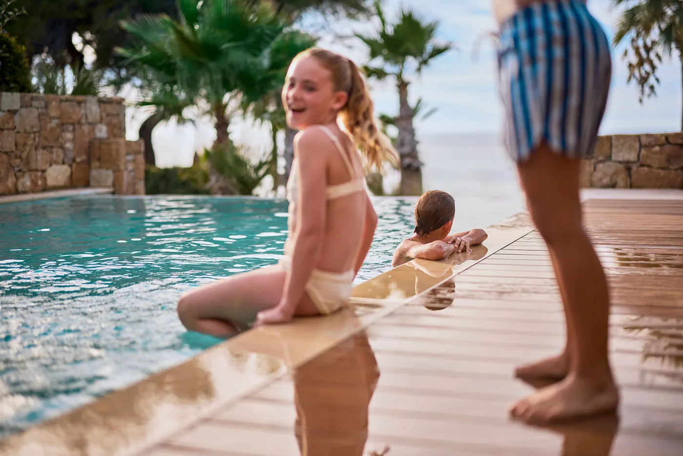 A child sitting on the edge of a pool beside a parent at Sani Resort