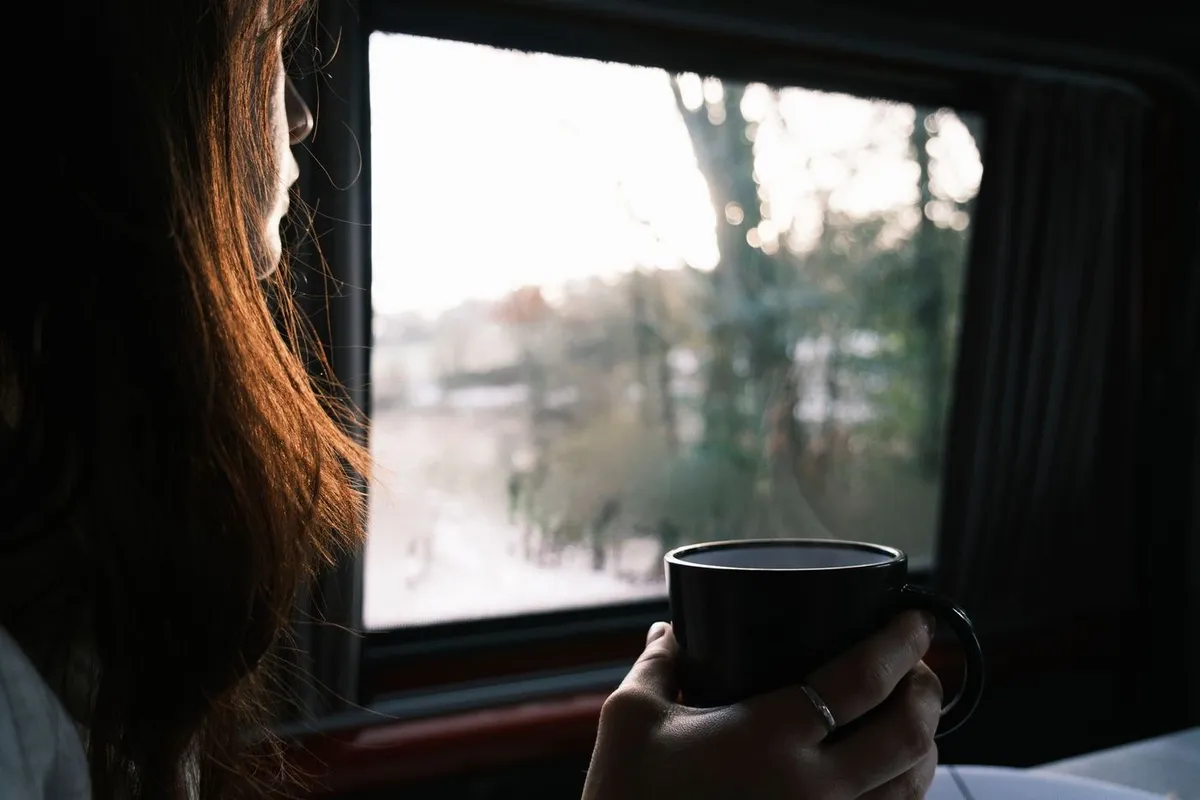A woman holding a mug and looking out of a window