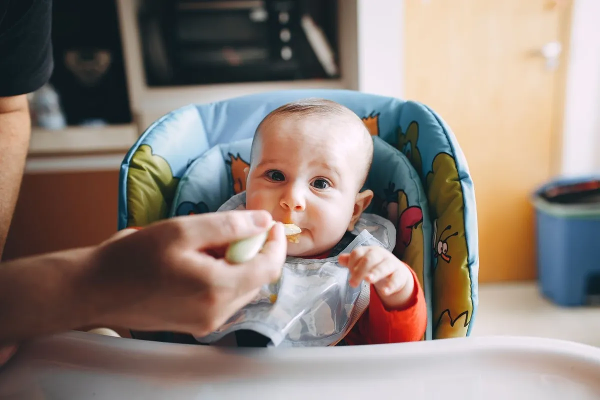 A parent spoon-feeding a smiling baby in a highchair