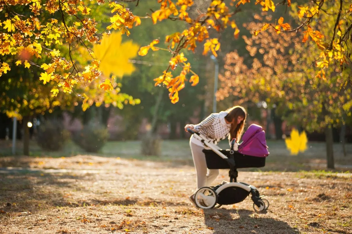 A mum walking with a pram through autumn leaves
