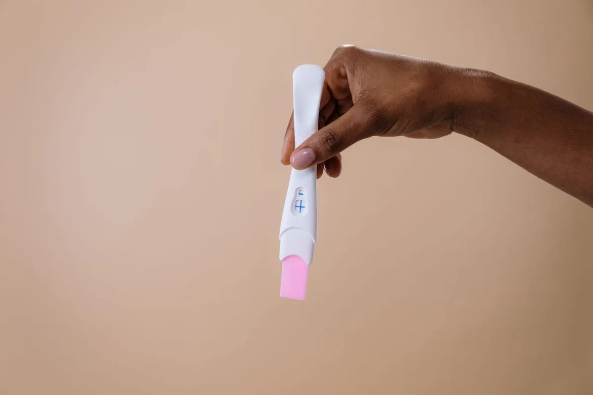 A hand holding a positive pregnancy test