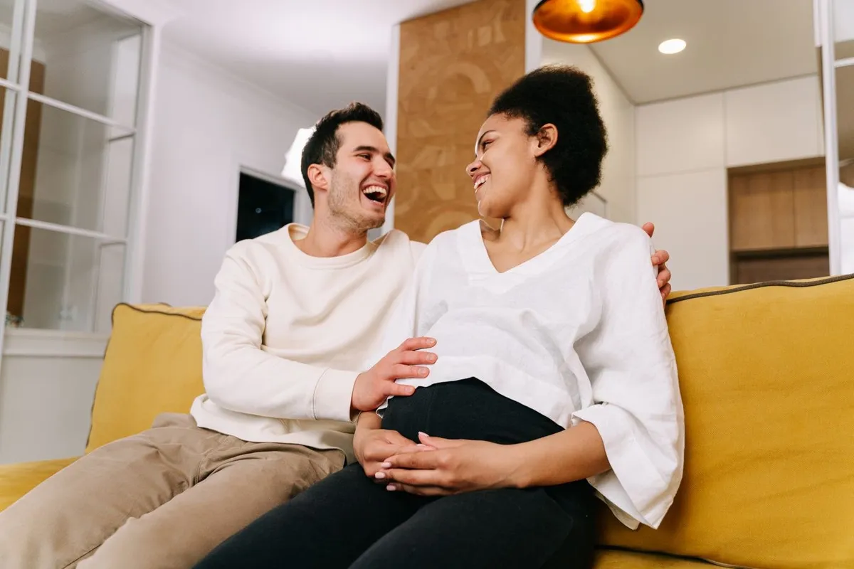An expectant couple laughing together on the sofa