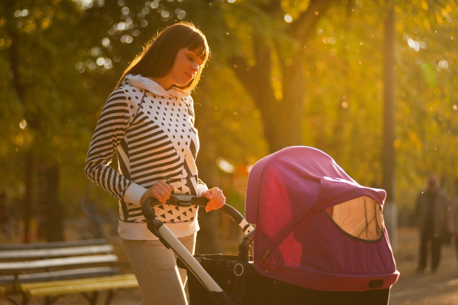 Mum pushing a pram through a sunlit park