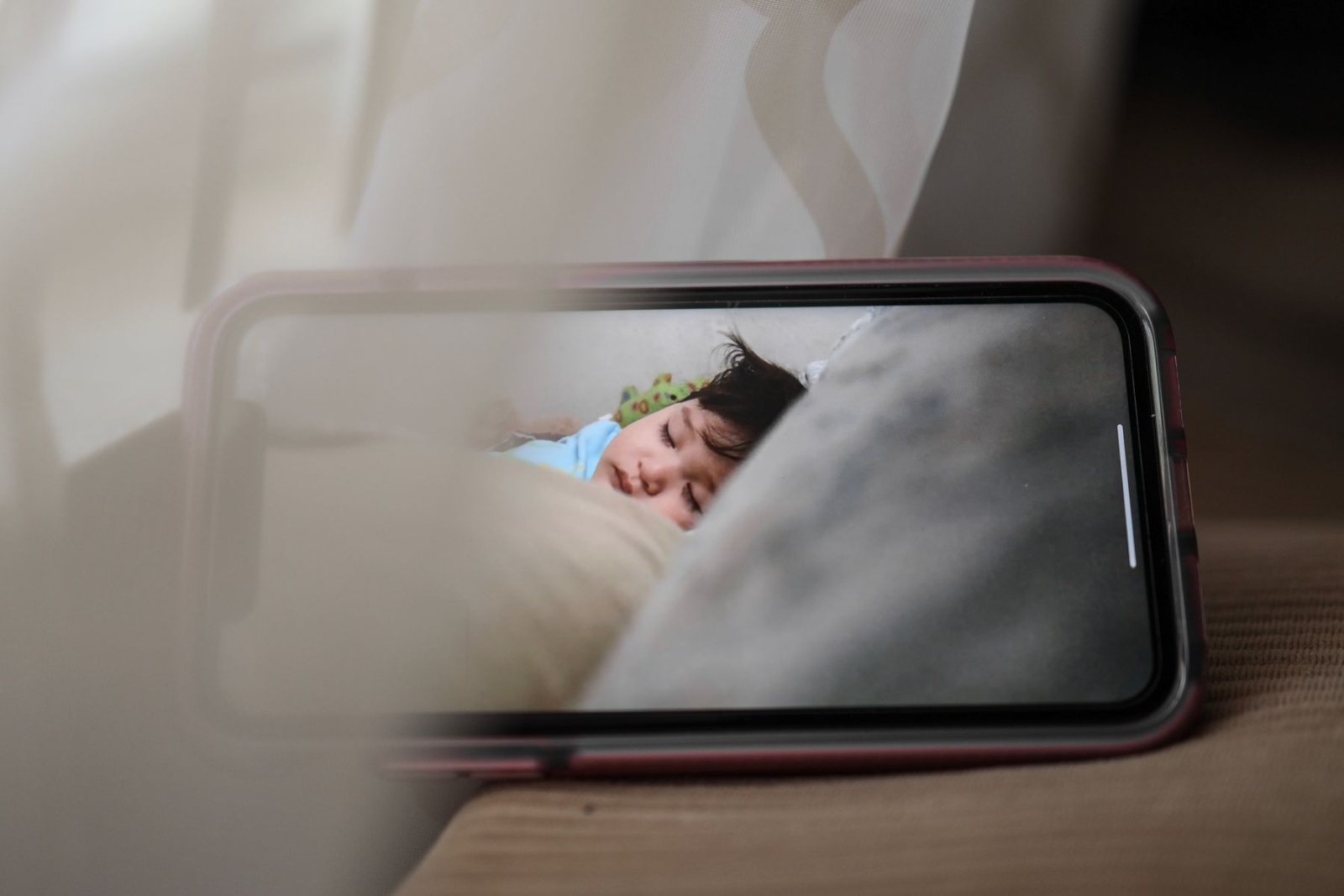 Smartphone showing a baby monitor video feed of a baby asleep in a cot