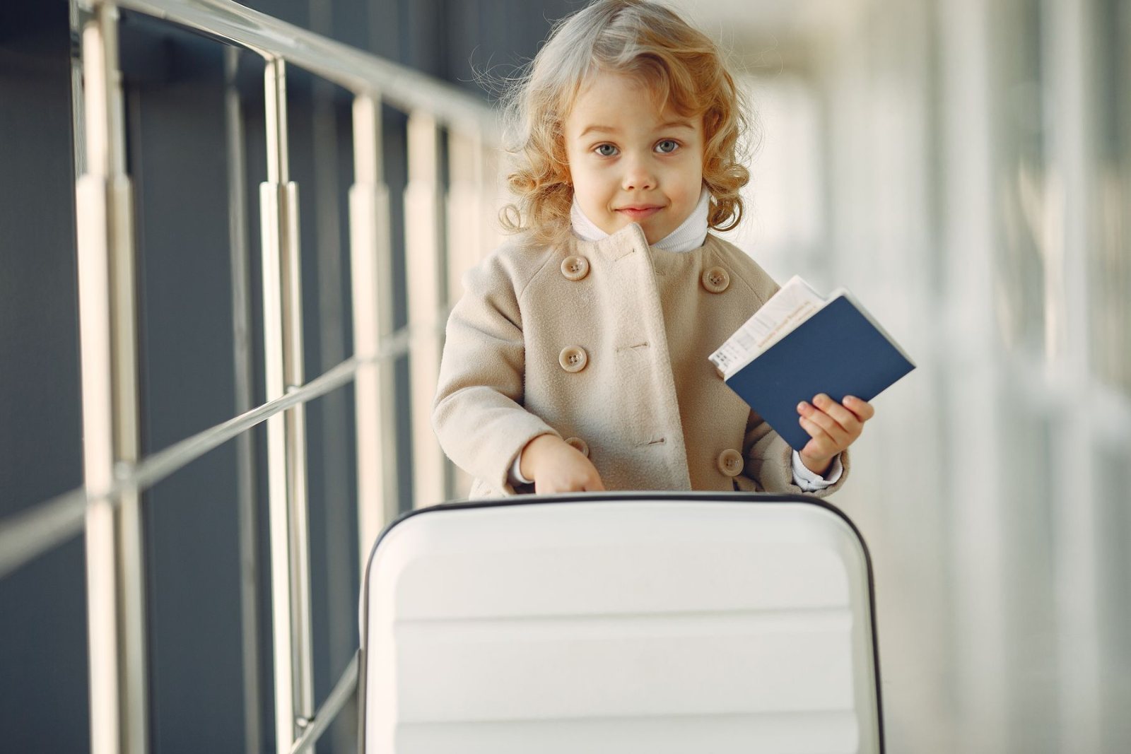 Toddler holding a passport next to a suitcase