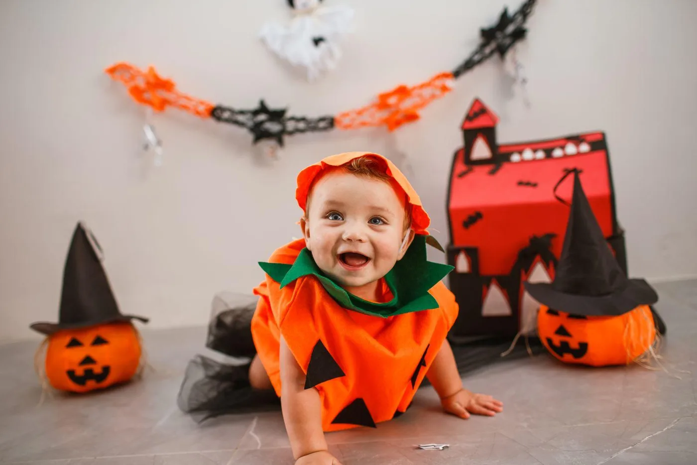 A happy baby in a pumpkin costume crawling across the floor