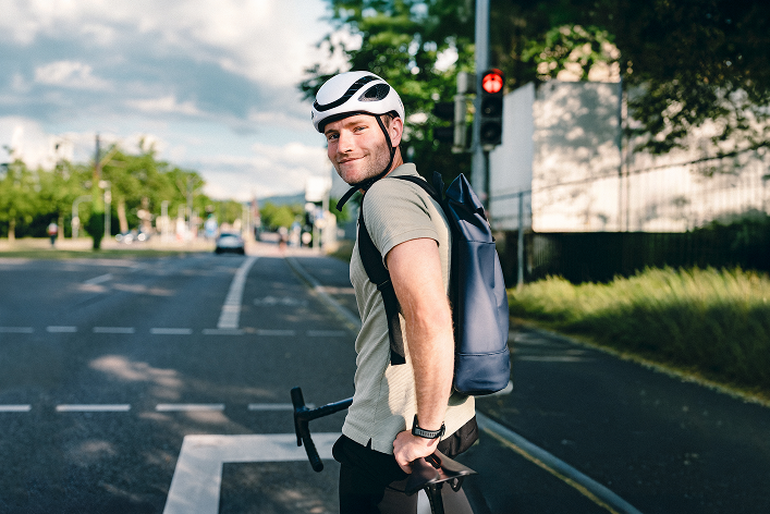 Ein Mitarbeiter der Haufe Group mit Fahrradhelm und Rucksack hält vor einer roten Ampel und blickt in die Kamera hinter sich.