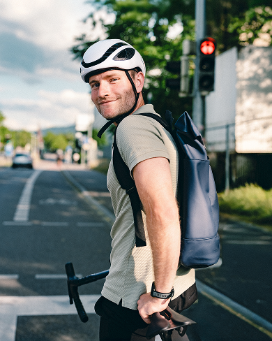 Ein Mitarbeiter der Haufe Group mit Fahrradhelm und Rucksack hält vor einer roten Ampel und blickt in die Kamera hinter sich.