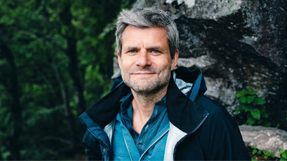 Raik Mickler, Konzerndatenschutzbeauftragter der Haufe Group, vor einer Felswand und dunklen Bäumen schaut in die Kamera.