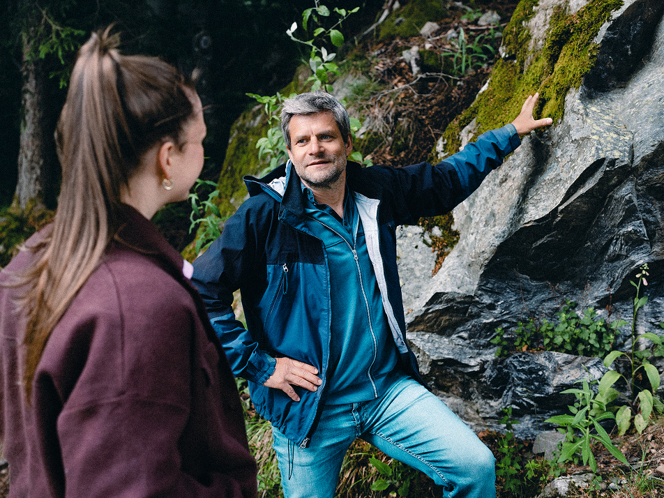 Nahaufnahme eines Farns und Raik Mickler, Konzerndatenschutzbeauftragter der Haufe Group, sowie eine Frau, die vor einer Felswand stehen.