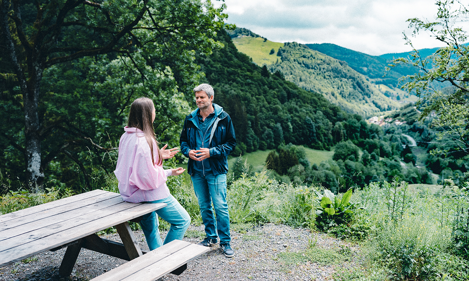 Raik Mickler, Konzerndatenschutzbeauftragter der Haufe Group, und eine Frau unterhalten sich an einem Vesperplatz in grüner Landschaft.