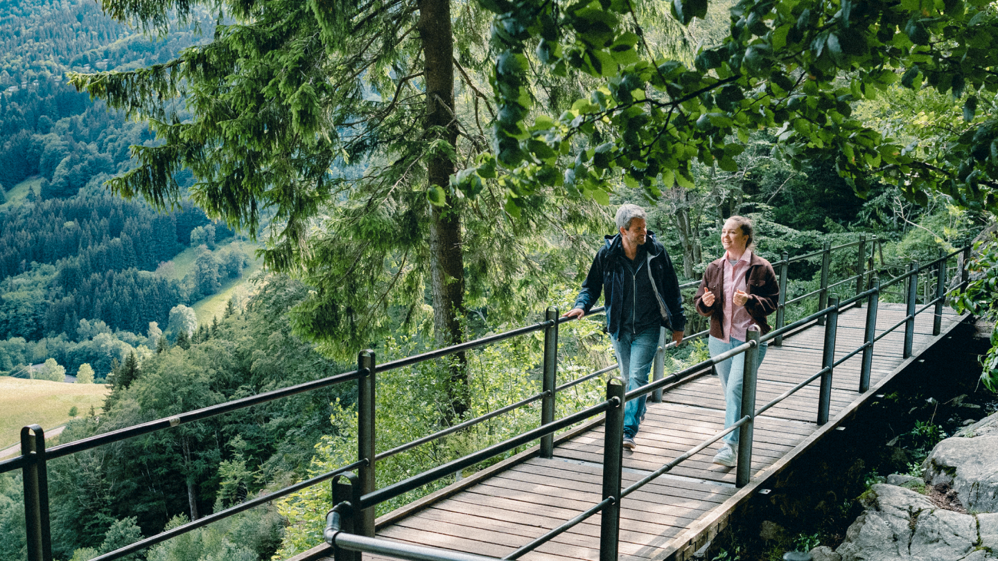 Raik Mickler, Konzerndatenschutzbeauftragter der Haufe Group, und eine Frau gehen über eine hölzerne Brücke in einem Waldgebiet.