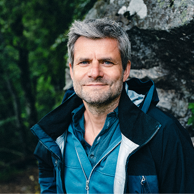 Raik Mickler, Konzerndatenschutzbeauftragter der Haufe Group, vor einer Felswand und dunklen Bäumen schaut in die Kamera.
