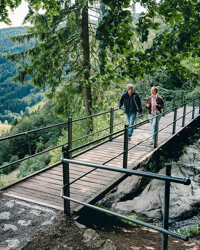 Raik Mickler, Konzerndatenschutzbeauftragter der Haufe Group, und eine Frau gehen über eine hölzerne Brücke in einem Waldgebiet.