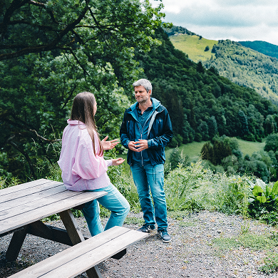 Raik Mickler, Konzerndatenschutzbeauftragter der Haufe Group, und eine Frau unterhalten sich an einem Vesperplatz in grüner Landschaft.