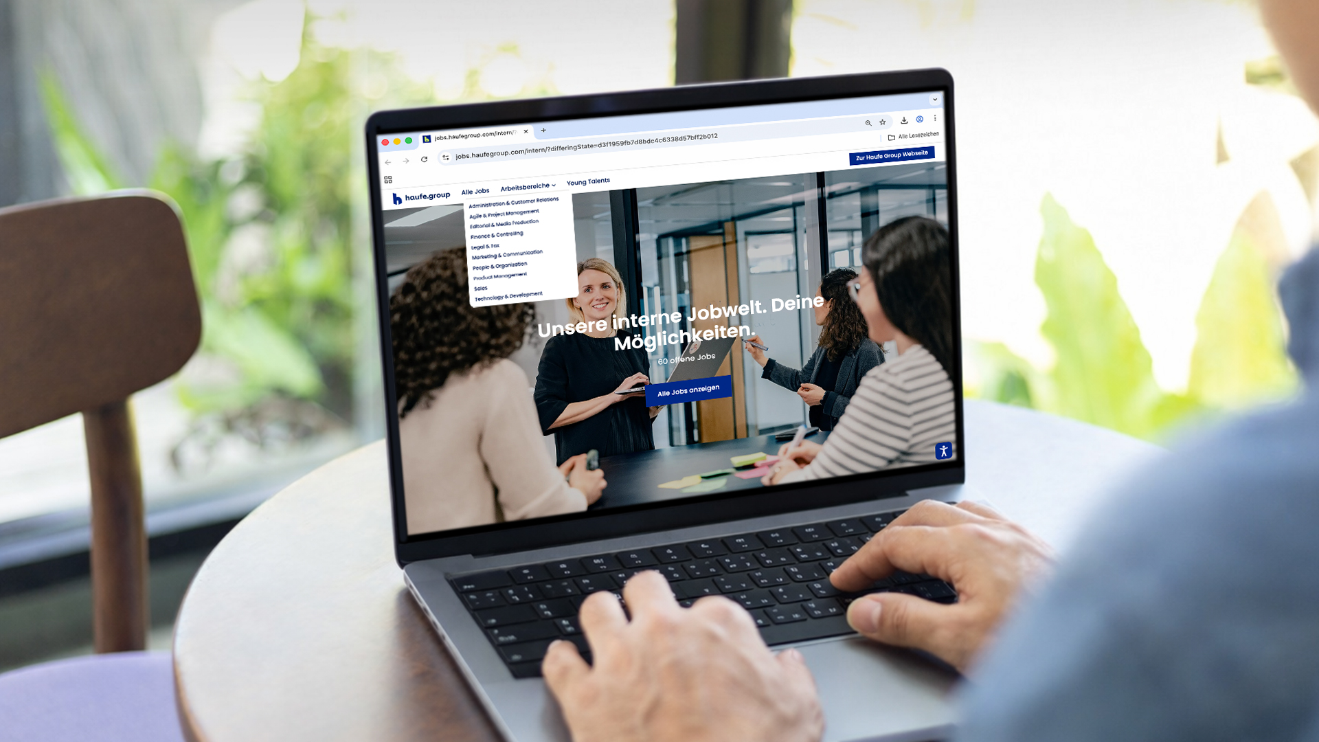Eine Person sitzt vor einem Computer. Auf dem Bildschirm ist die interne Jobbörse der Haufe Group geöffnet. Auf dem Screen steht "Unsere interne Jobwelt. Deine Möglichkeiten."