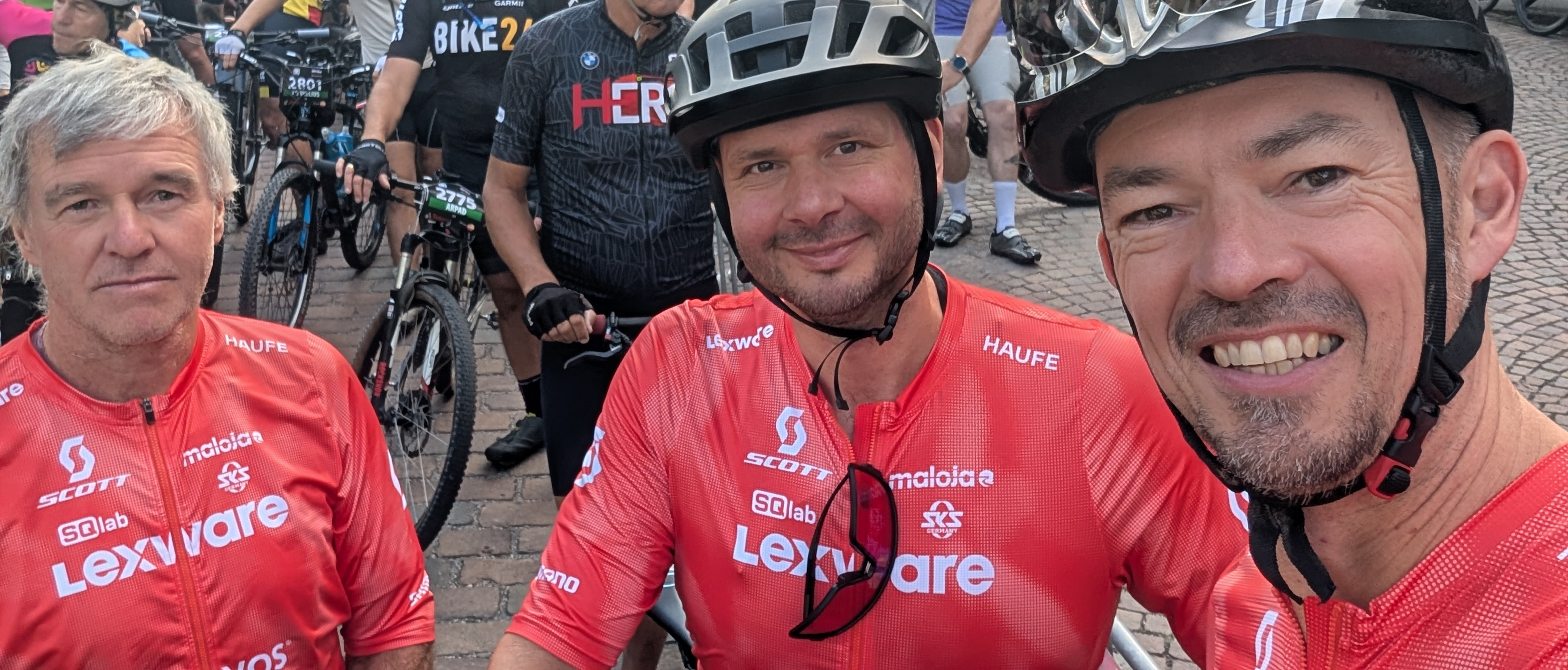 Johannes ist beim Start des Ultra Bike Marathons in Kirchzarten mit zwei Kollgen zu sehen. Alle drei tragen ein rotes Trikot und lächeln in die Kamera.