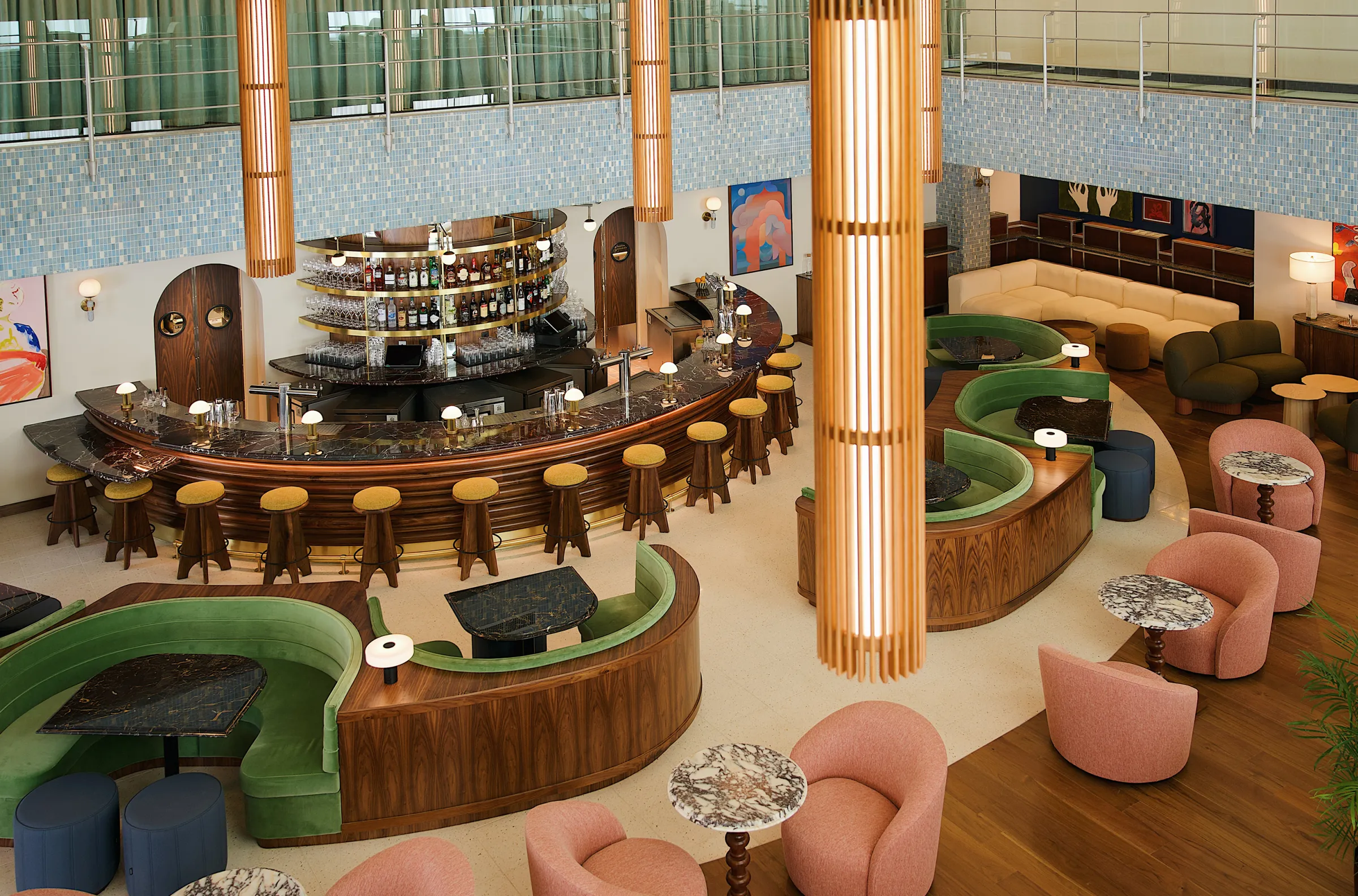 Mid-century modern bar with curved green booths, marble tables, and soft pink chairs in a bright, stylish lounge setting.