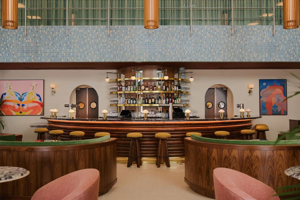 A long bar with stools is centered in a room with a tiled wall and artwork on the sides.