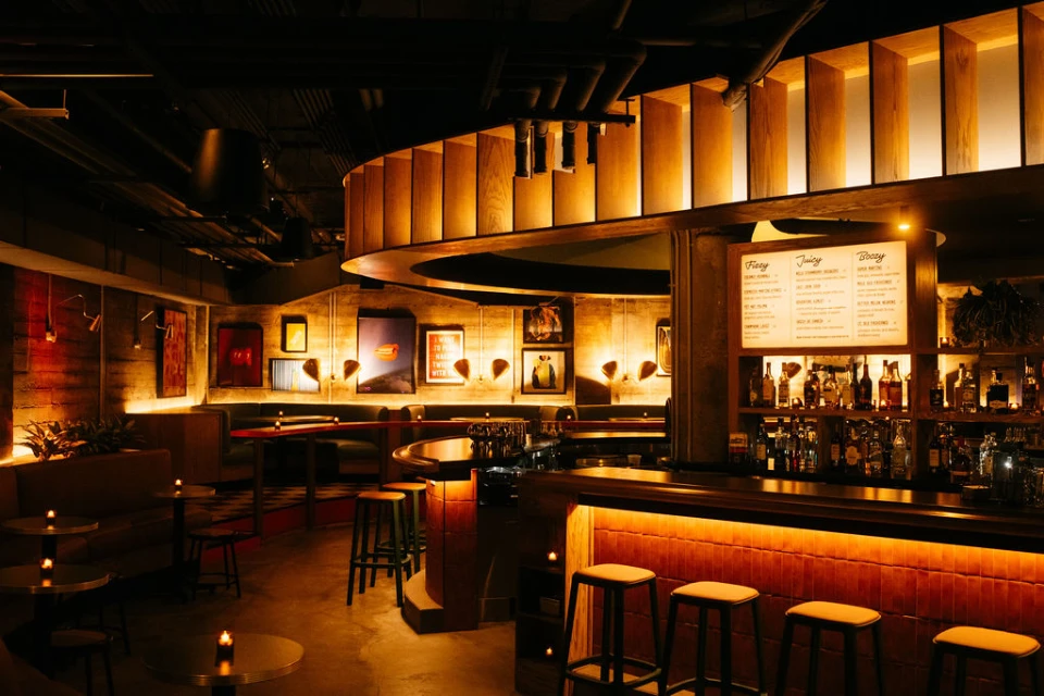 A dark, dimly lit room featuring a circular bar with ambient light and several pillars.