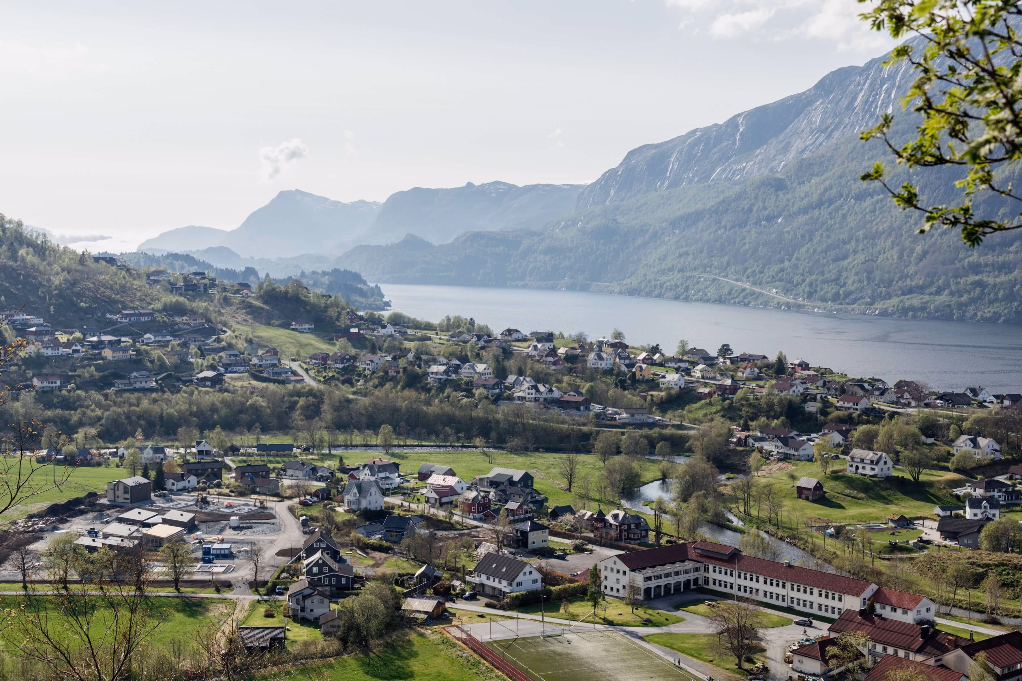 Landsby med flere hus ved en innsjø og fjell i bakgrunnen på en overskyet dag.