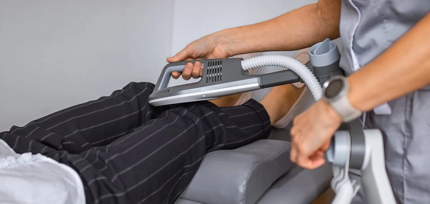 Пацієнт проходить сеанс суперіндуктивної магнітотерапії, під час якого медпрацівник тримає апарат для подачі потужного магнітного поля на область ніг.