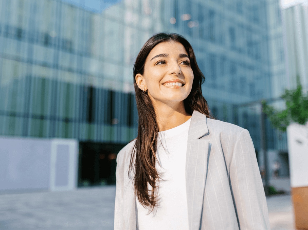 A pretty young woman, standing outside in a city, smiles with beautiful, healthy teeth after pulp revascularization at the best endodontist in Mountain View