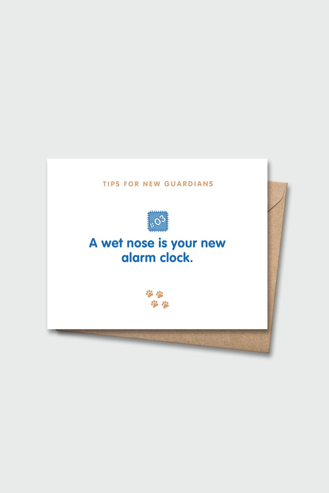 Letterpressed greeting card with wooden block and paw prints illustrations, the words "tips for new guardians: a wet nose is your new alarm clock" on white background, and taupe envelope