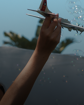Hand holding a toy airplane against a blue sky with bubbles floating nearby.