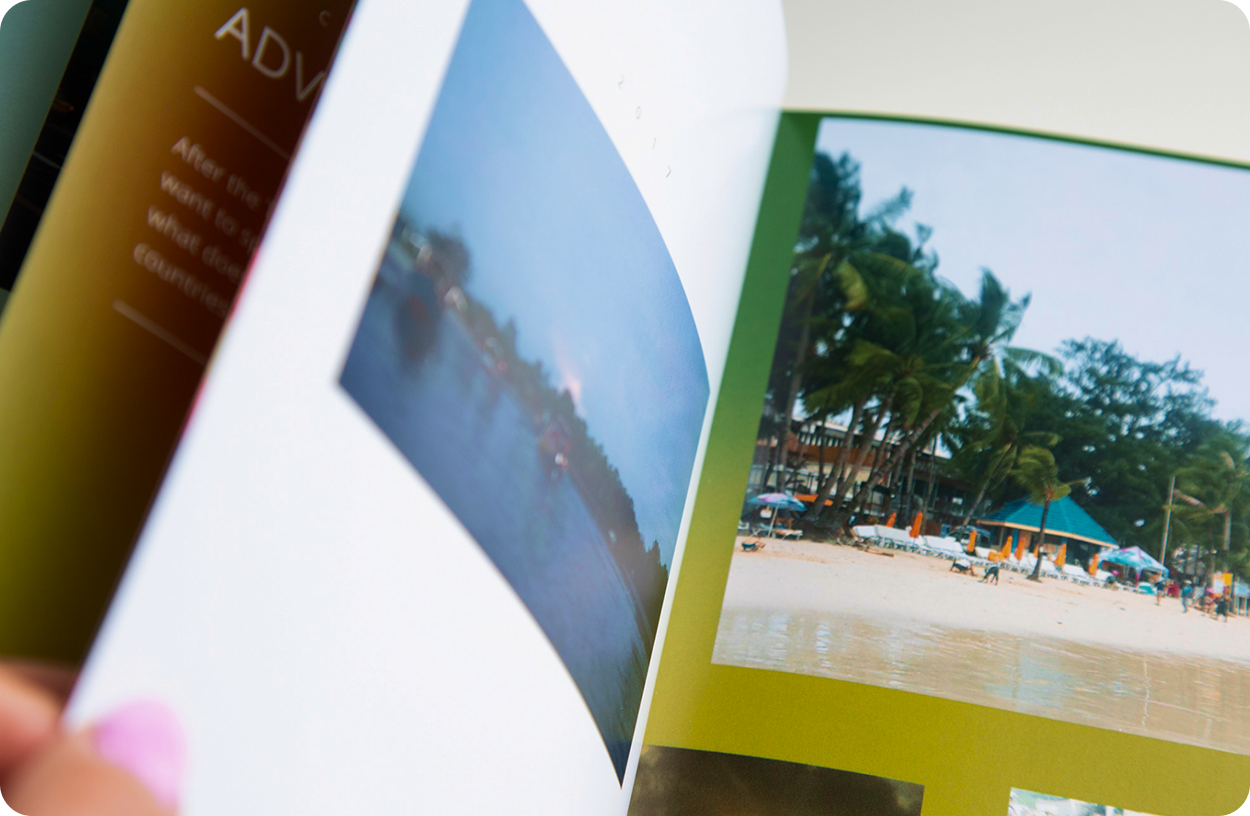 Close-up of a person flipping through a travel photo book featuring beach and sunset images.