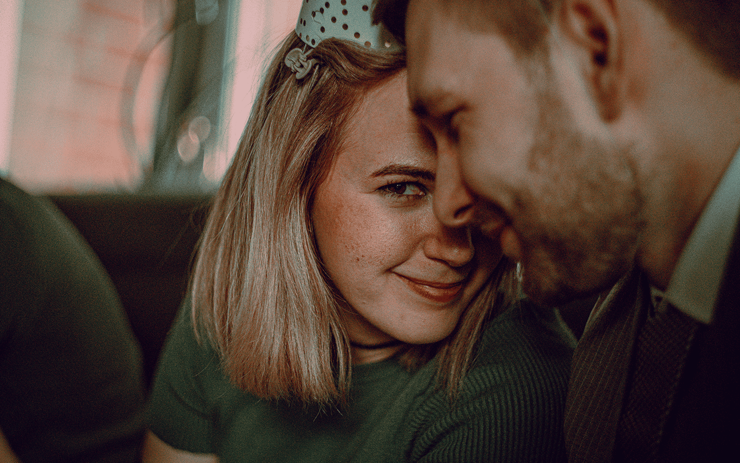 Portrait of woman smiling mischievously into the camera, in front of her is a man's face out of focus