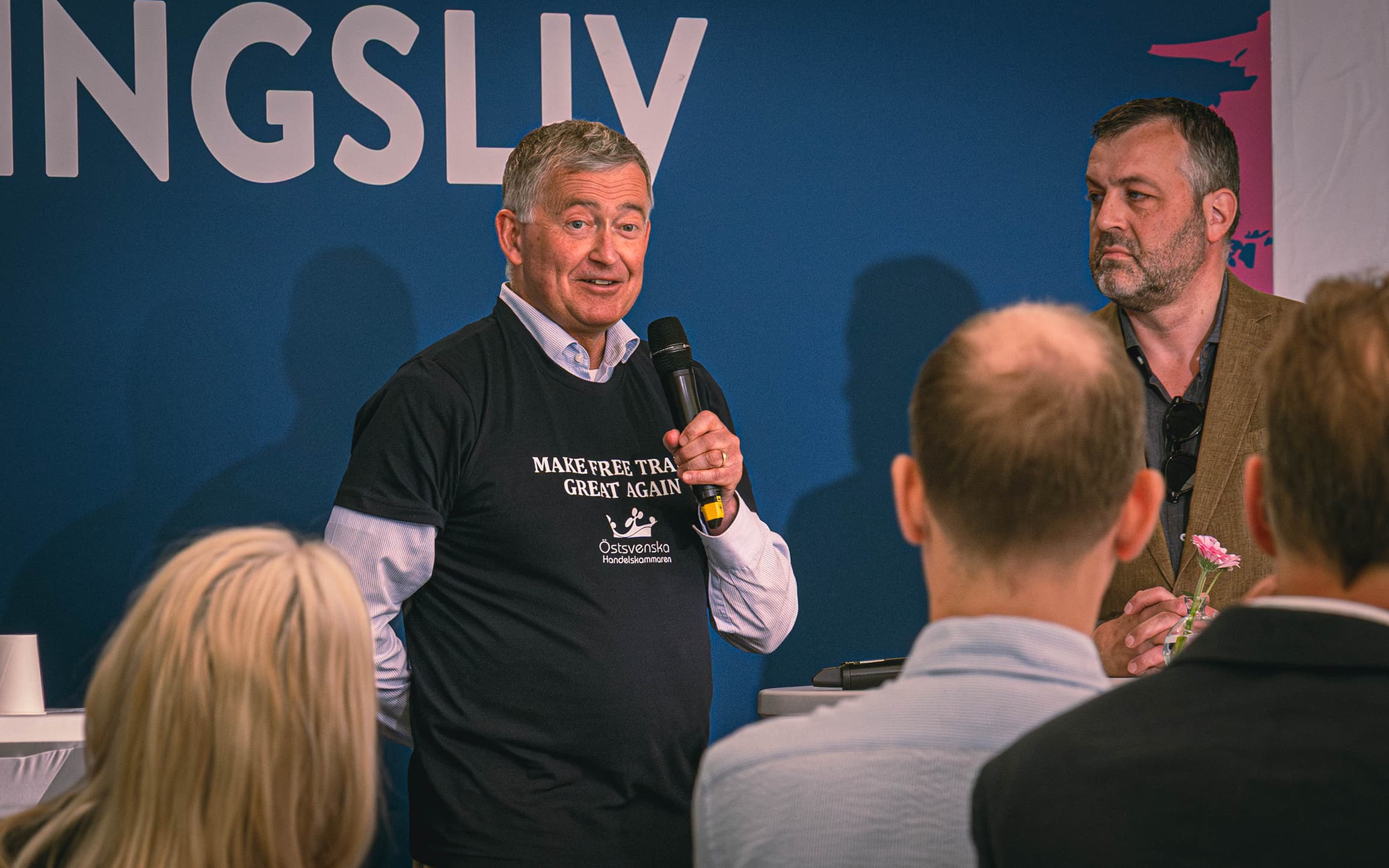 Director General Anders Ahnlid in t-shirt that says Östsvenska Handelskammaren Make Free Trade Great Again at Almedalen, speaking in front of audience