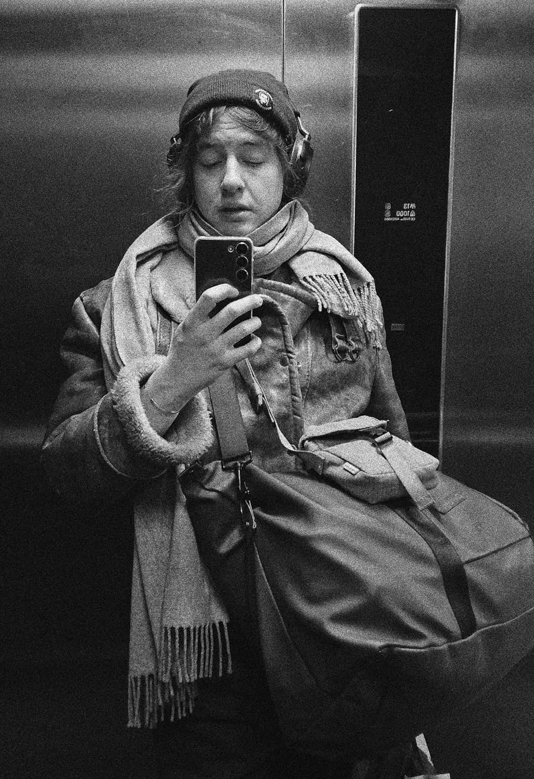 Young person with medium-length brown hair, wearing a blue and white striped button-up shirt and a chain necklace, looking at the camera.