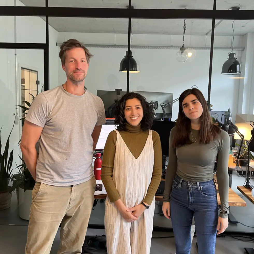 Three colleagues from Berlin Bytes are in the office and smile into the camera