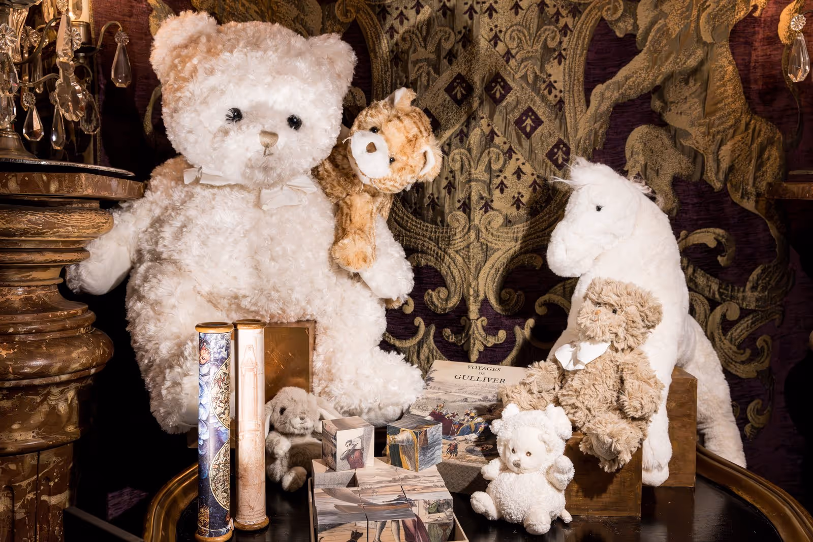 Collection de peluches comprenant plusieurs ours, une licorne blanche, un petit lapin, des livres anciens et des cubes illustrés sur une table.