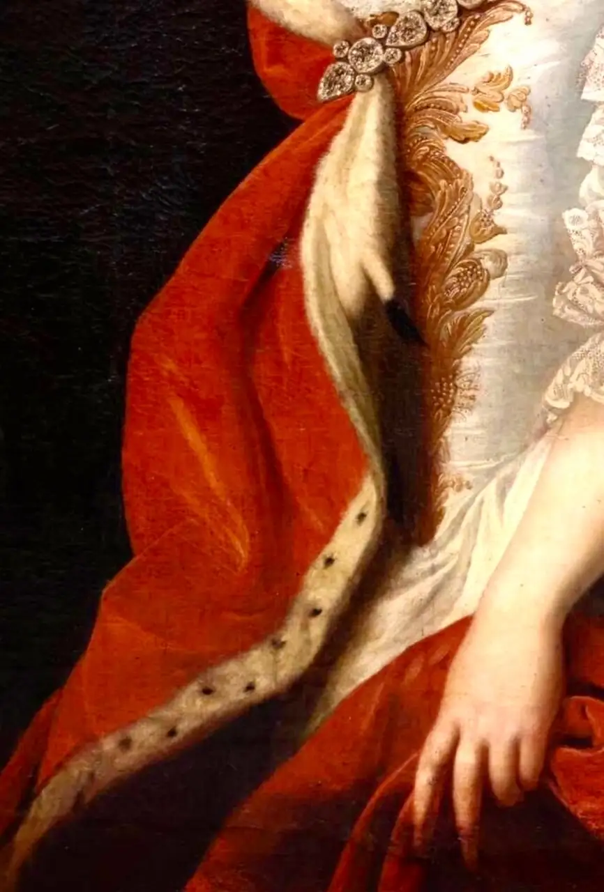 Détail d'une robe rouge avec doublure en fourrure blanche et broderies dorées sur un corsage blanc.