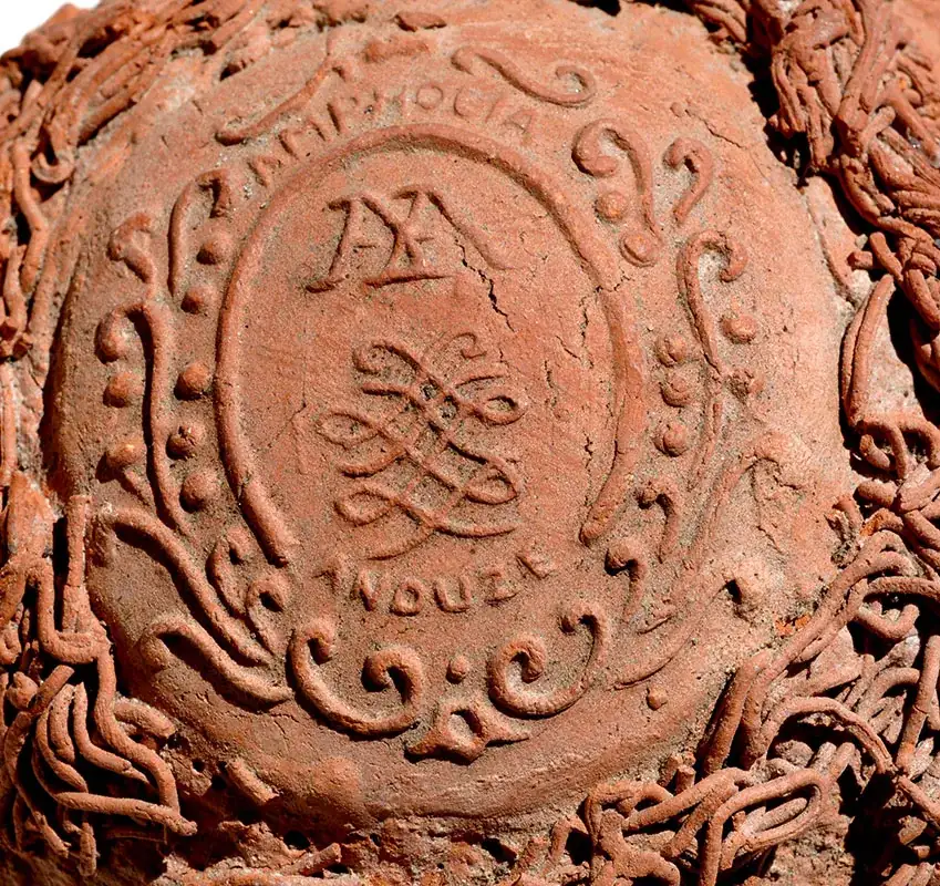 Détail d'une amphore en terre cuite ornée de motifs sculptés et d'inscriptions circulaires.
