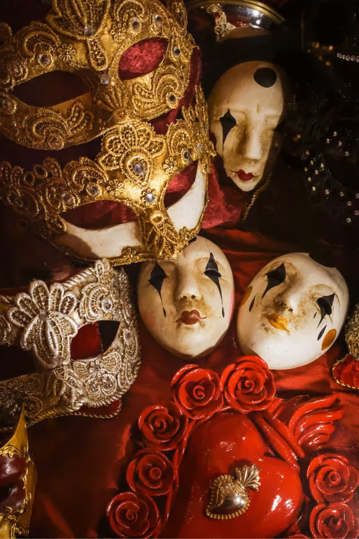 Masques vénitiens dorés et blancs avec détails en dentelle et visages peints, sur fond rouge.