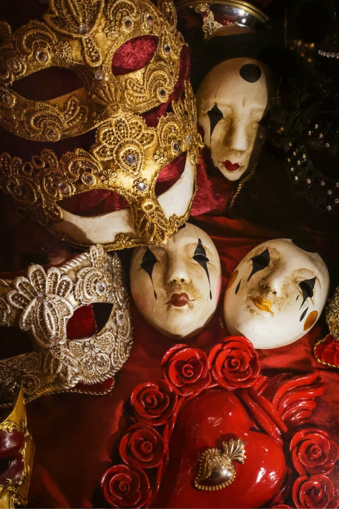 Masques vénitiens dorés et blancs avec détails en dentelle et visages peints, sur fond rouge.