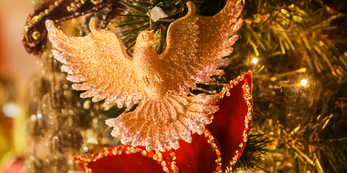 Ornement de colombe dorée brillante suspendu à un sapin de Noël décoré de feuilles rouges pailletées.