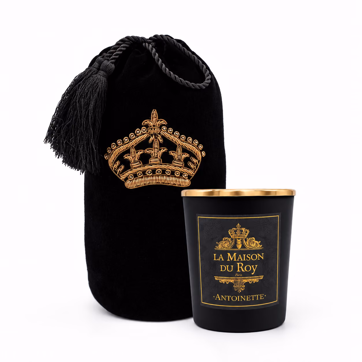 Bougie noire avec couvercle doré, étiquette dorée indiquant « La Maison du Roy Paris Antoinette », à côté d'une pochette noire en velours ornée d'une couronne dorée brodée et dotée d'un cordon à pompon.