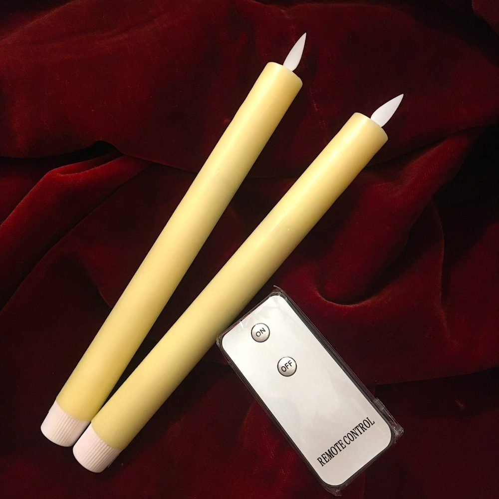 Deux bougies ivoire à piles avec flamme LED et télécommande, posées sur velours rouge